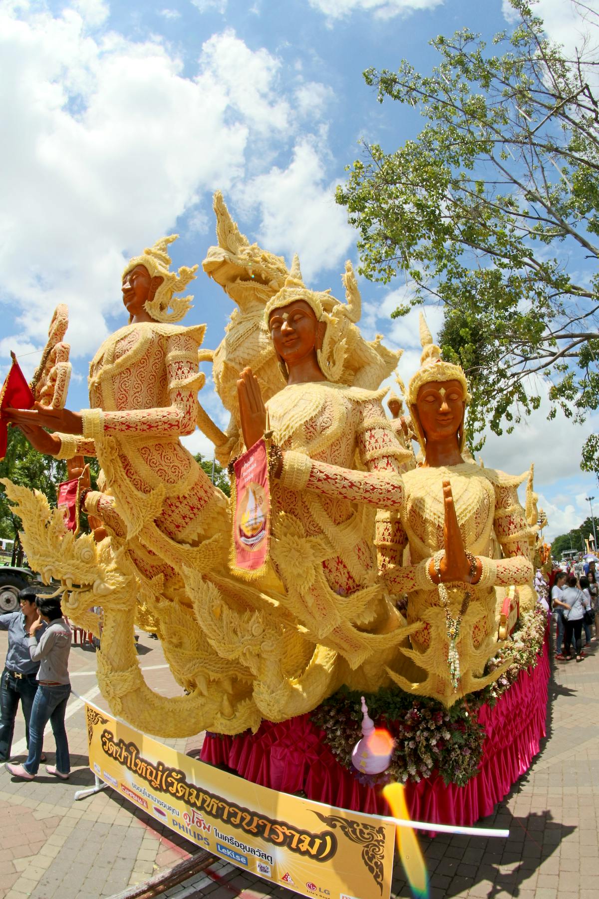 A large ornate parade float with sculpted figures and gilded detailing photographed against a blue sky during a street festival