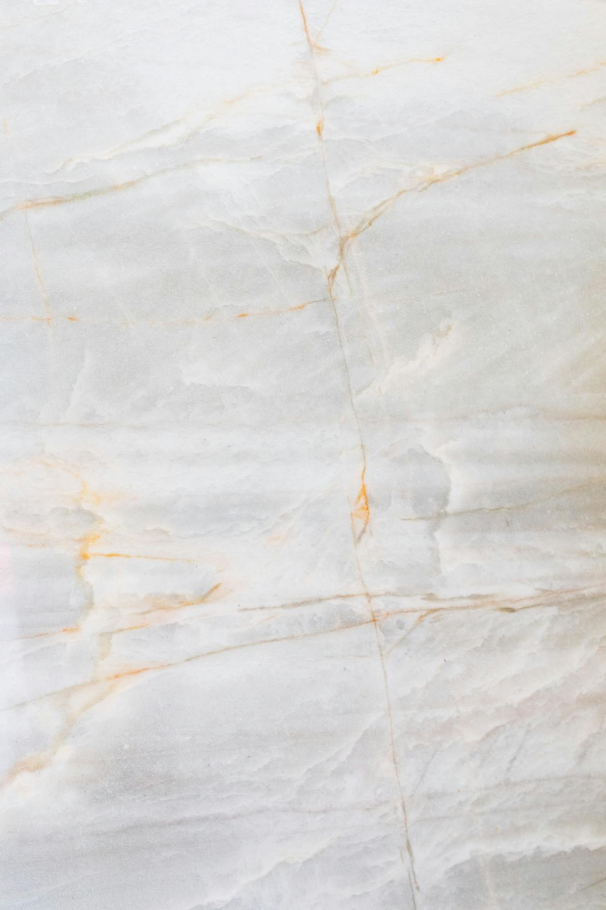 Close-up of polished white Carrara marble surface with faint grey and rust-orange veining running across the slab