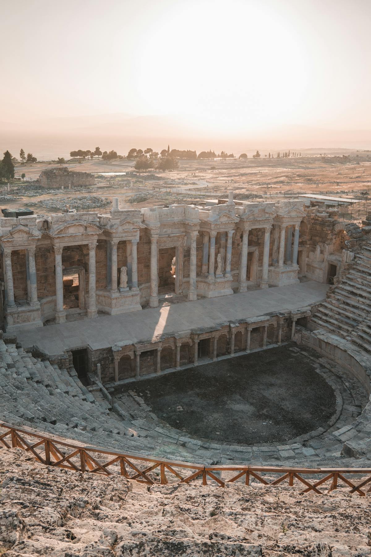 An outdoor stone amphitheatre at golden hour, banked rows of seats facing an open performance area under a dusk sky